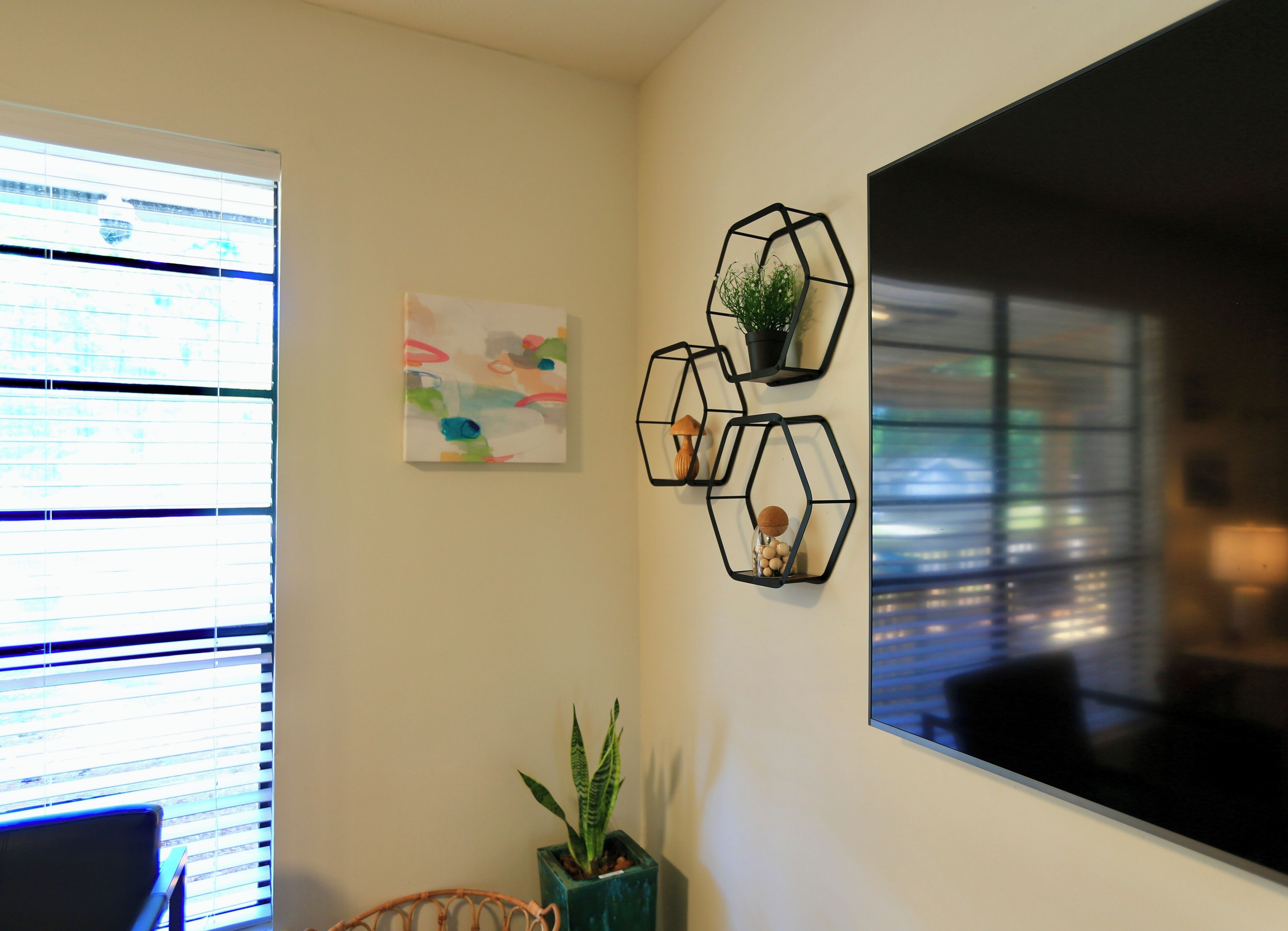 A room with a large window, a wall-mounted abstract painting, and three hexagonal wall decorations with plants.