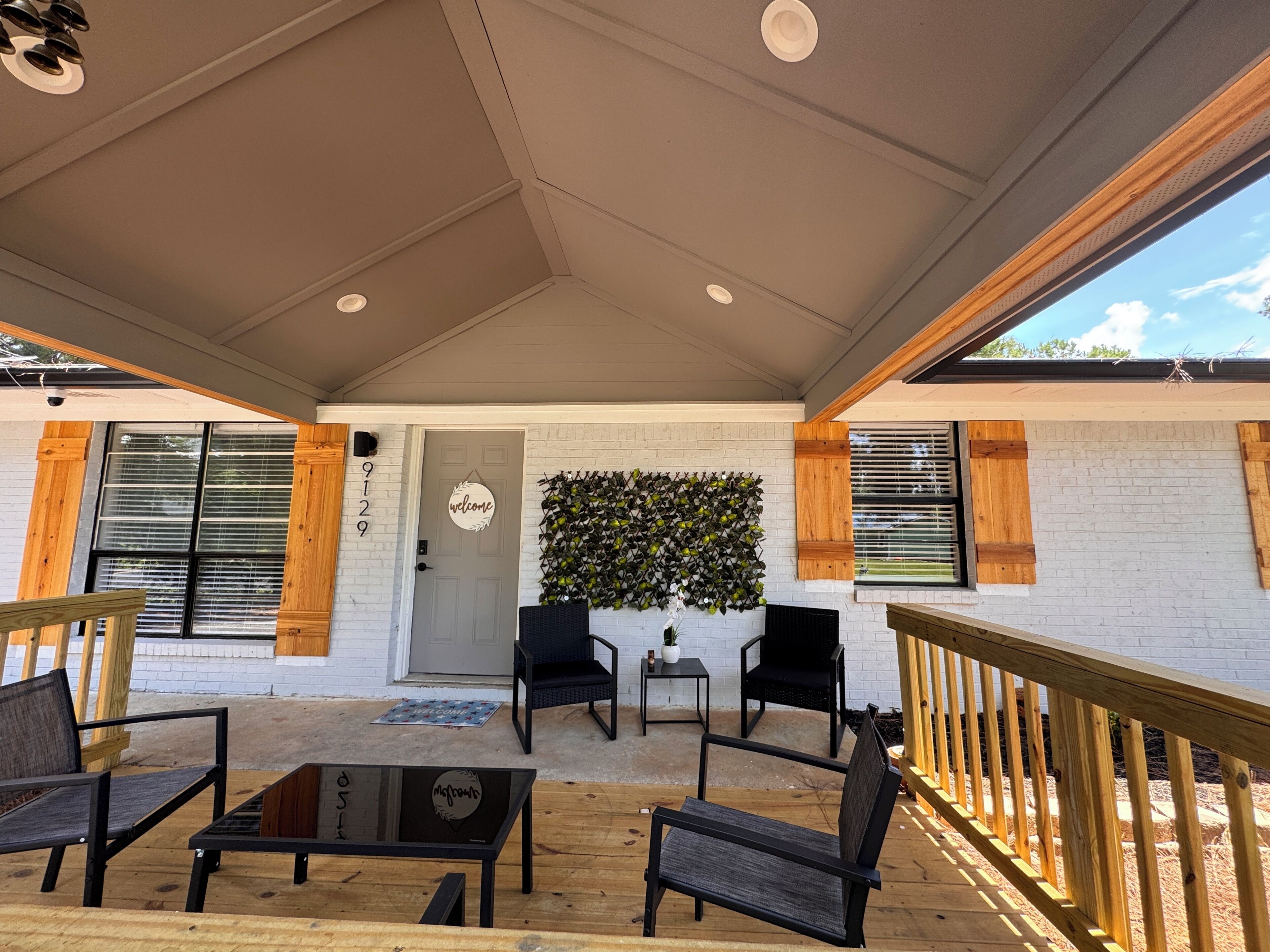 A covered patio area with seating, a welcome sign, and a wall-mounted plant display.