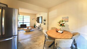 A modern kitchen with a stainless steel refrigerator, a dining area with a round wooden table and cushioned chairs, and a living room with a sofa and a TV mounted on the wall. - Family-Friendly Covington Escape w/ Fenced Backyard, Full Kitchen & Coffee Bar (Covington)