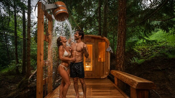 A wooden cabin with a showerhead, a wooden deck, and a forested backdrop.