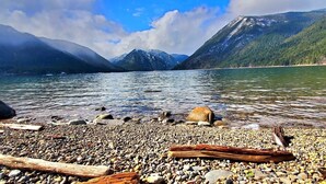 A pebbled beach with clear water, surrounded by mountains.