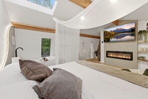 Ein Schlafzimmer mit Bett, Kamin, großem Fenster und einem Gemälde einer Berglandschaft.