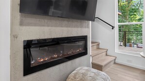 A modern living room with a fireplace, a flat-screen TV mounted above it, and a staircase leading to an upper level.