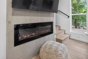 Ein modernes Wohnzimmer mit Kamin, einem flachbildfernseher darüber und einer Treppe, die zu einer oberen Ebene führt.