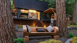 A cabin with a wooden deck, a bench with cushions, and a staircase leading to an upper level.