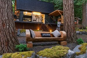 Eine Hütte mit einer Holzterrasse, einer Bank mit Kissen und einer Treppe zu einer oberen Ebene.