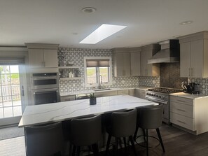 A modern kitchen with a central island, bar stools, built-in ovens, a large window, and a skylight. - Poolside Estate (Dubuque)
