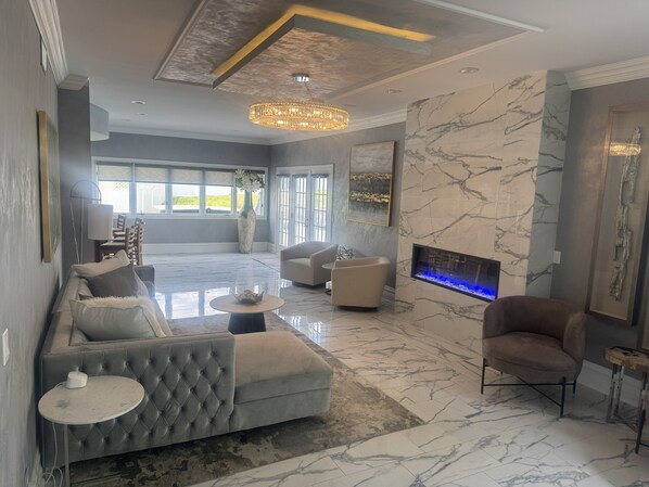 A modern living room with a sectional sofa, armchairs, a round coffee table, a fireplace, and a large window. - Poolside Estate (Dubuque)