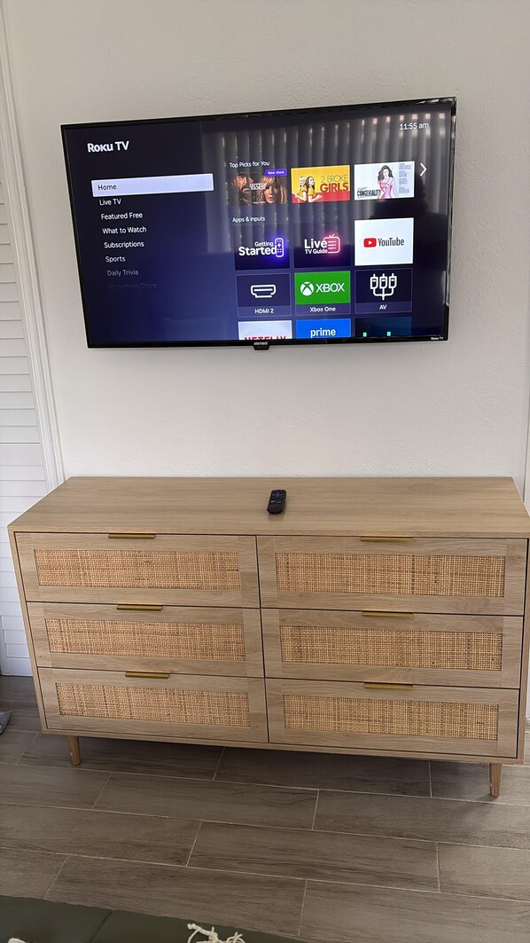 A Roku TV mounted on a wall displaying various streaming services and a wooden cabinet below. - Fantastic 1-bedroom townhome with AC in vibrant Miami (Miami)