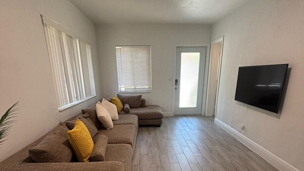A living room with a sectional sofa, a flat-screen TV, and a door leading to another room. - Fantastic 1-bedroom townhome with AC in vibrant Miami (Miami)