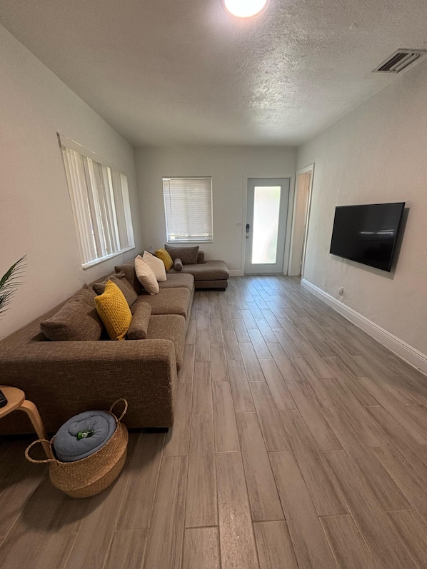 Una sala de estar con un sofá modular, un televisor de pantalla plana y una puerta que da a otra habitación.