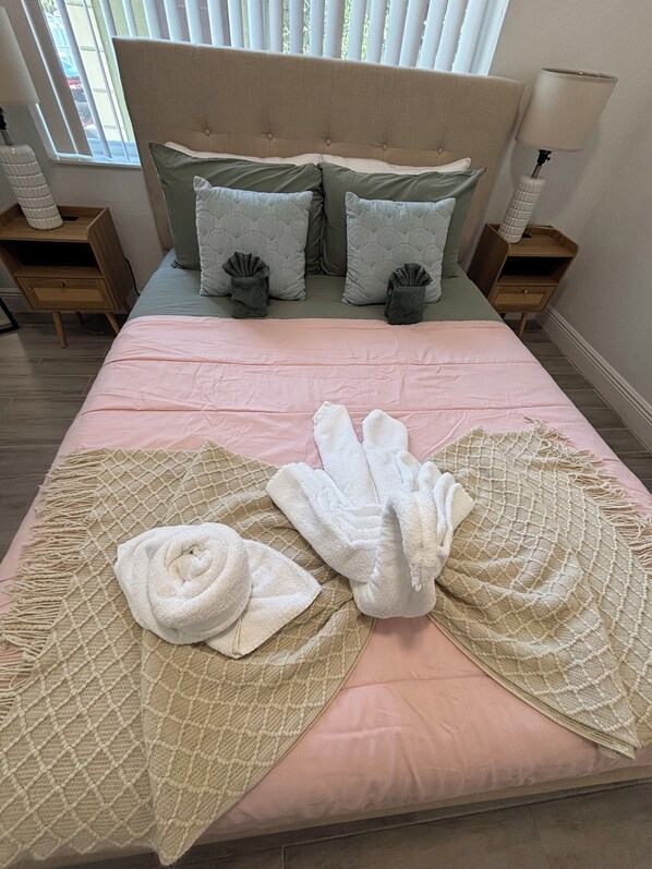 A neatly made bed with a pink bedspread, two grey pillows, and a beige throw blanket.