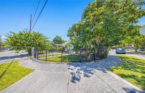 A fenced property with a paved driveway, trees, and a clear sky. - Fantastic 1-bedroom townhome with AC in vibrant Miami (Miami)
