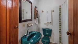 A bathroom with a wooden door, a green sink, a toilet, a mirror, and a towel rack.