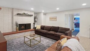 A living room with a fireplace, a brown sofa, a glass coffee table, and a view of a car through an open door.