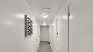 A hallway with white walls, a carpeted floor, and a ceiling with recessed lighting.