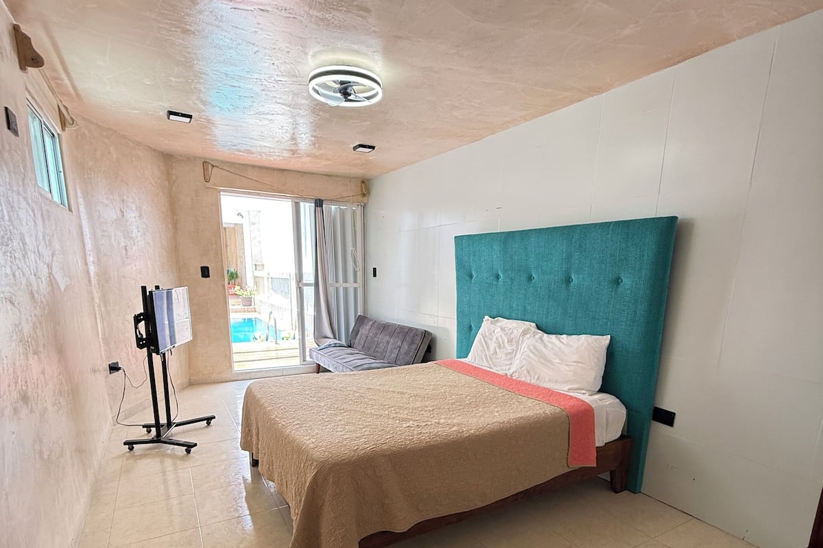 A hotel room with a bed, a desk, a chair, a TV, and a window.