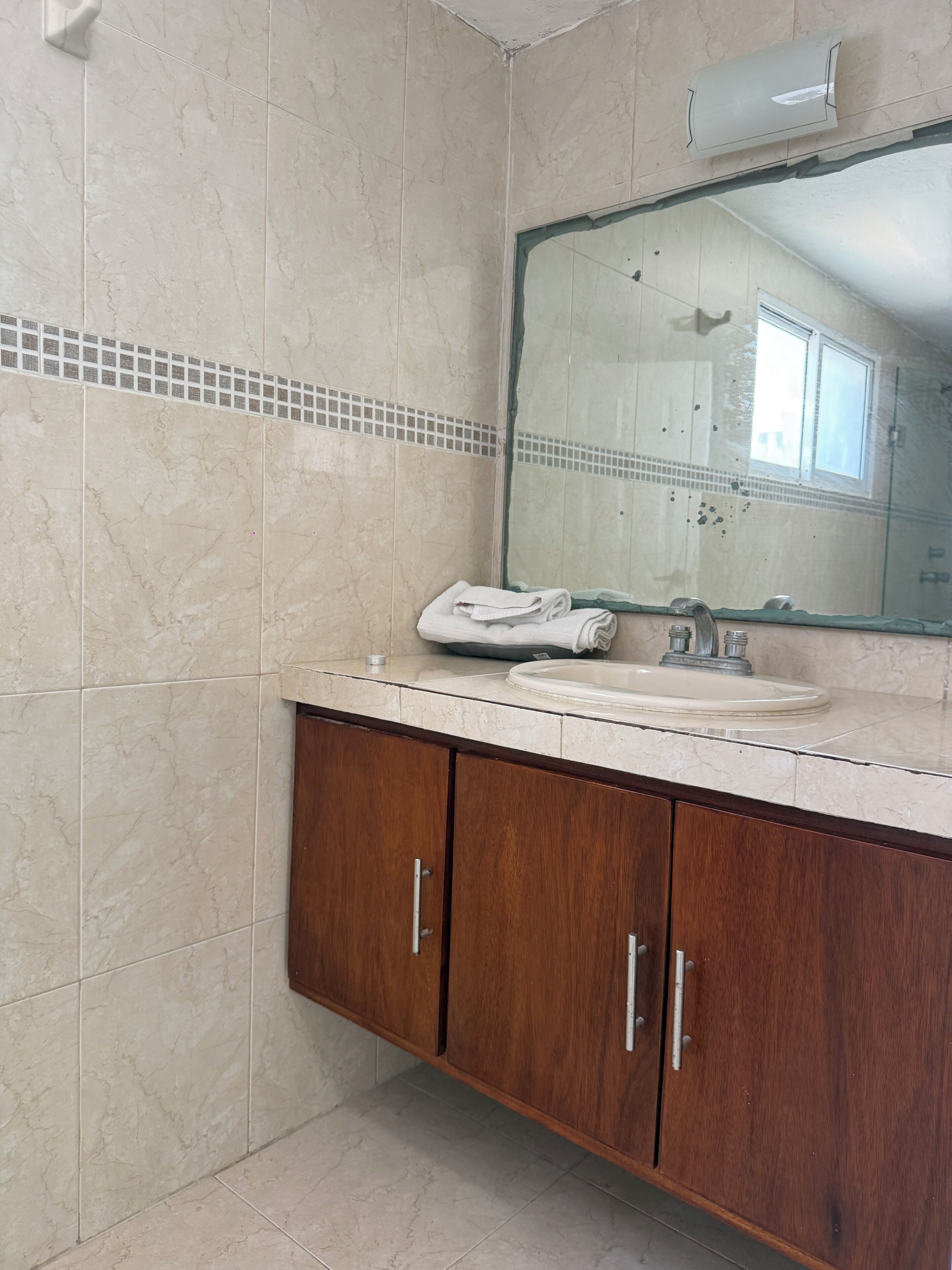 A bathroom with a marble floor, a sink with a mirror above it, and wooden cabinets.
