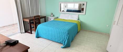 Una habitación con cama, escritorio, silla, ventana con cortinas, equipo de aire acondicionado y un espejo en la pared.