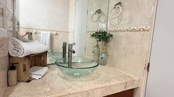 Un baño con un lavamanos de vidrio, un espejo, un toallero y una planta.