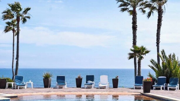 A poolside area with lounge chairs and palm trees, overlooking the ocean. - Wonderful 3-bedroom house in Las Gaviotas perfect for your getaway (Las Gaviotas)