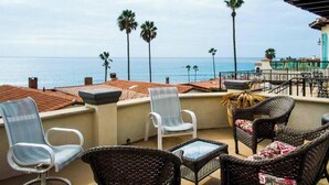 A furnished balcony with wicker furniture, a view of the sea, and a building with a tiled roof. - Wonderful 3-bedroom house in Las Gaviotas perfect for your getaway (Las Gaviotas)