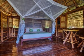 A wooden room with a bed, a table, and a mosquito net. - Eden Yoga & Wellness Resort (San Juan del Sur)