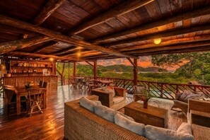An outdoor wooden deck with wicker furniture, a bar area, and a view of a lush landscape. - Eden Yoga & Wellness Resort (San Juan del Sur)