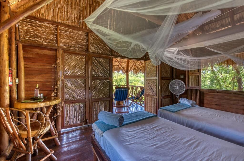 A wooden cabin with two beds, a fan, and a table with a bottle.
