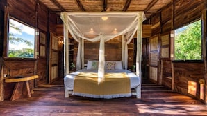 A wooden room with a bed under a canopy, a small table, and a window with a view of trees. - Eden Yoga & Wellness Resort (San Juan del Sur)
