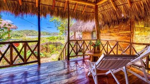 A thatched-roof structure with a wooden deck, a table, and a chair. - Eden Yoga & Wellness Resort (San Juan del Sur)