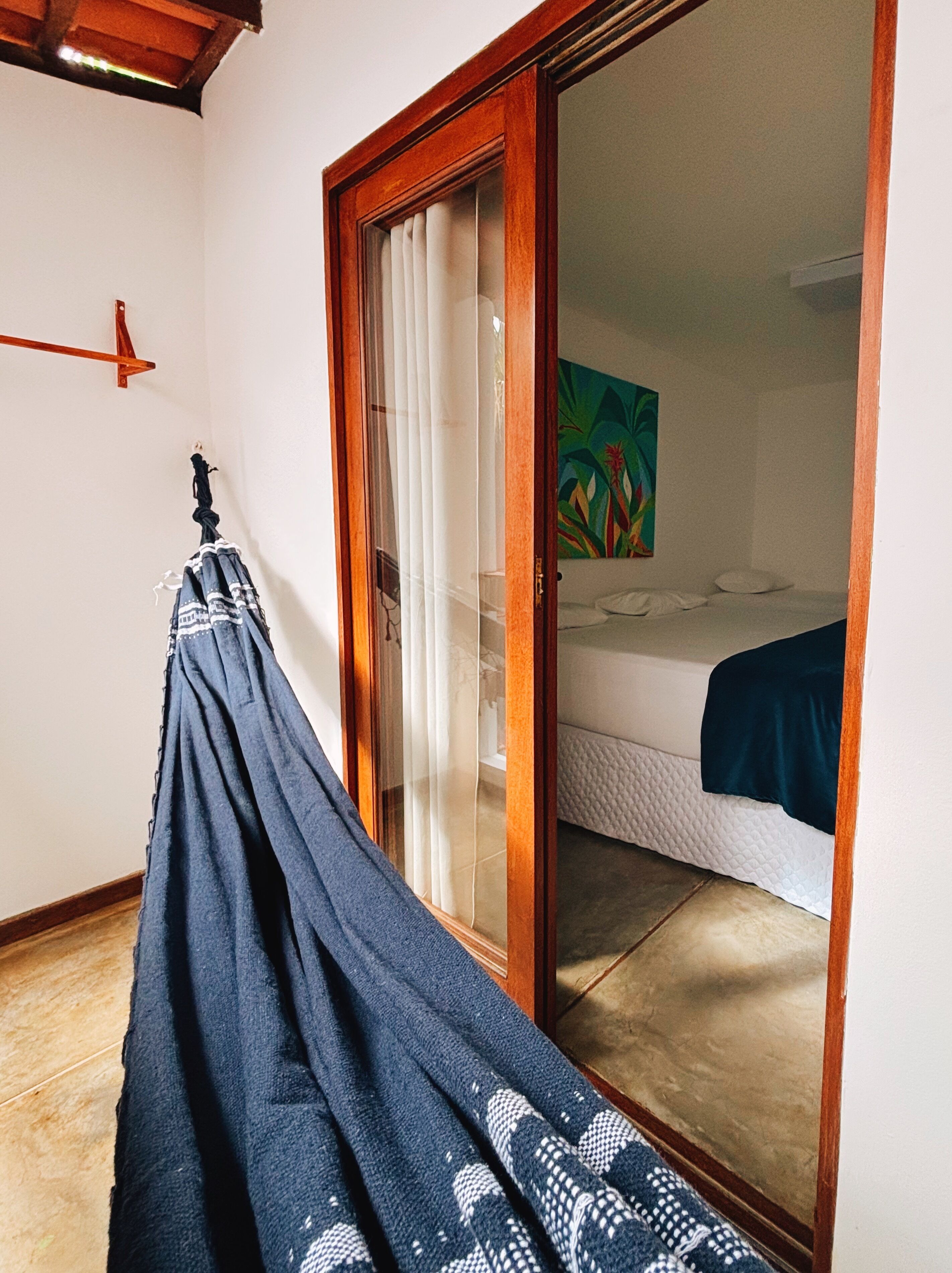 A room with a bed, a sliding glass door, a painting, and a hanging towel.