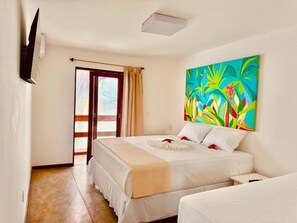 A hotel room with a bed, a TV mounted on the wall, a window with curtains, and a colorful painting on the wall.