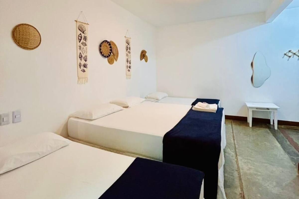 A hotel room with two beds, a small table, a wall-mounted mirror, and decorative wall hangings.