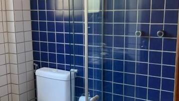 Un baño con cabina de ducha de vidrio, inodoro y paredes con azulejos azules.