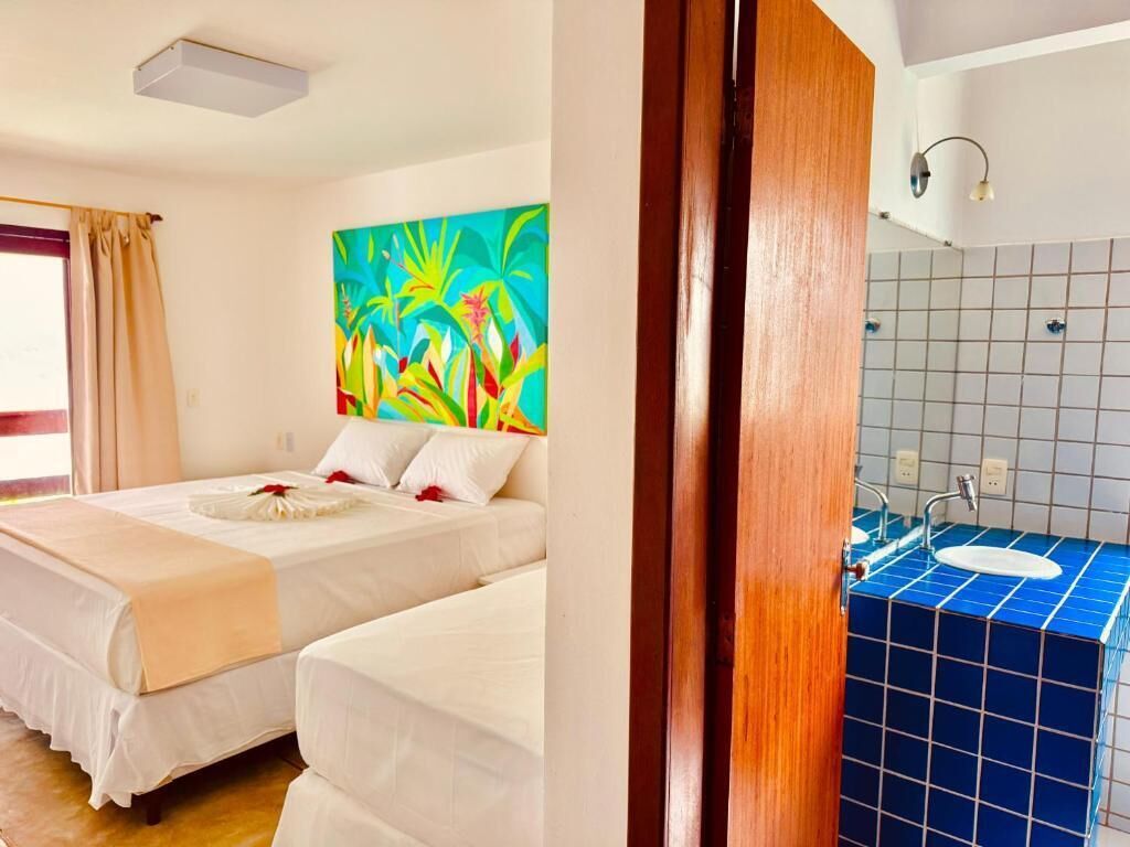 A hotel room with two beds, a colorful painting, a bathroom with blue tiles, and a wooden door.