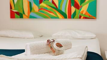 Een hotelkamer met een bed, een keurig opgevouwen witte handdoek en een kleurrijk schilderij met een tropisch thema aan de muur.