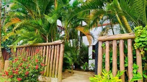 Un sendero serpentea por un exuberante jardín con valla de madera y plantas tropicales.