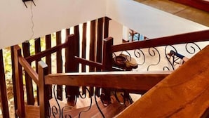 Una escalera de madera con barandilla, una lámpara colgante y un ventanal con vistas al verdor.