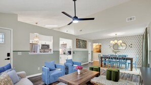Ein geräumiger Wohnbereich mit Esstisch, blauen Stühlen, einer Couch und einem Deckenventilator.