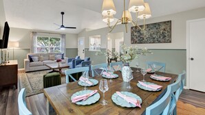 Ein Essbereich mit einem Holztisch, gedeckt für sechs Personen, flankiert von blauen Stühlen, einer Chandelüster und einer Vase mit Blumen.