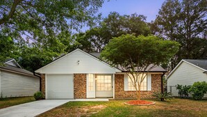 Einbungalow mit Garage, Backsteinanteil und Rasen mit Baum.