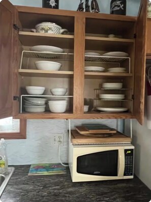 Eine Küche mit einer Mikrowelle auf der Arbeitsfläche, Holzschränken mit Geschirr und einem kleinen Regal mit einem dekorativen Gegenstand.
