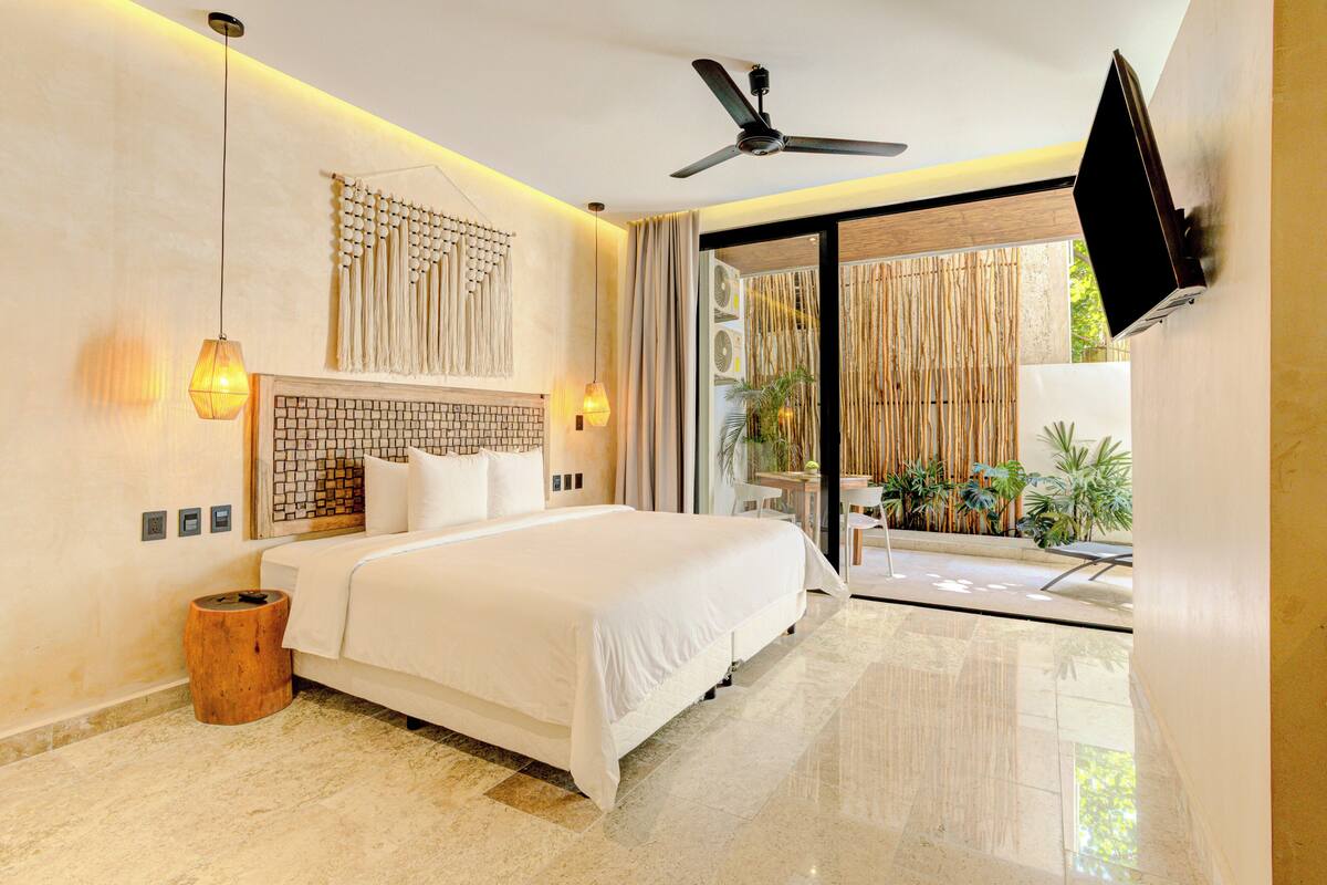 Quarto de hotel moderno com cama, ventoinha no teto, televisão e vista para o exterior.