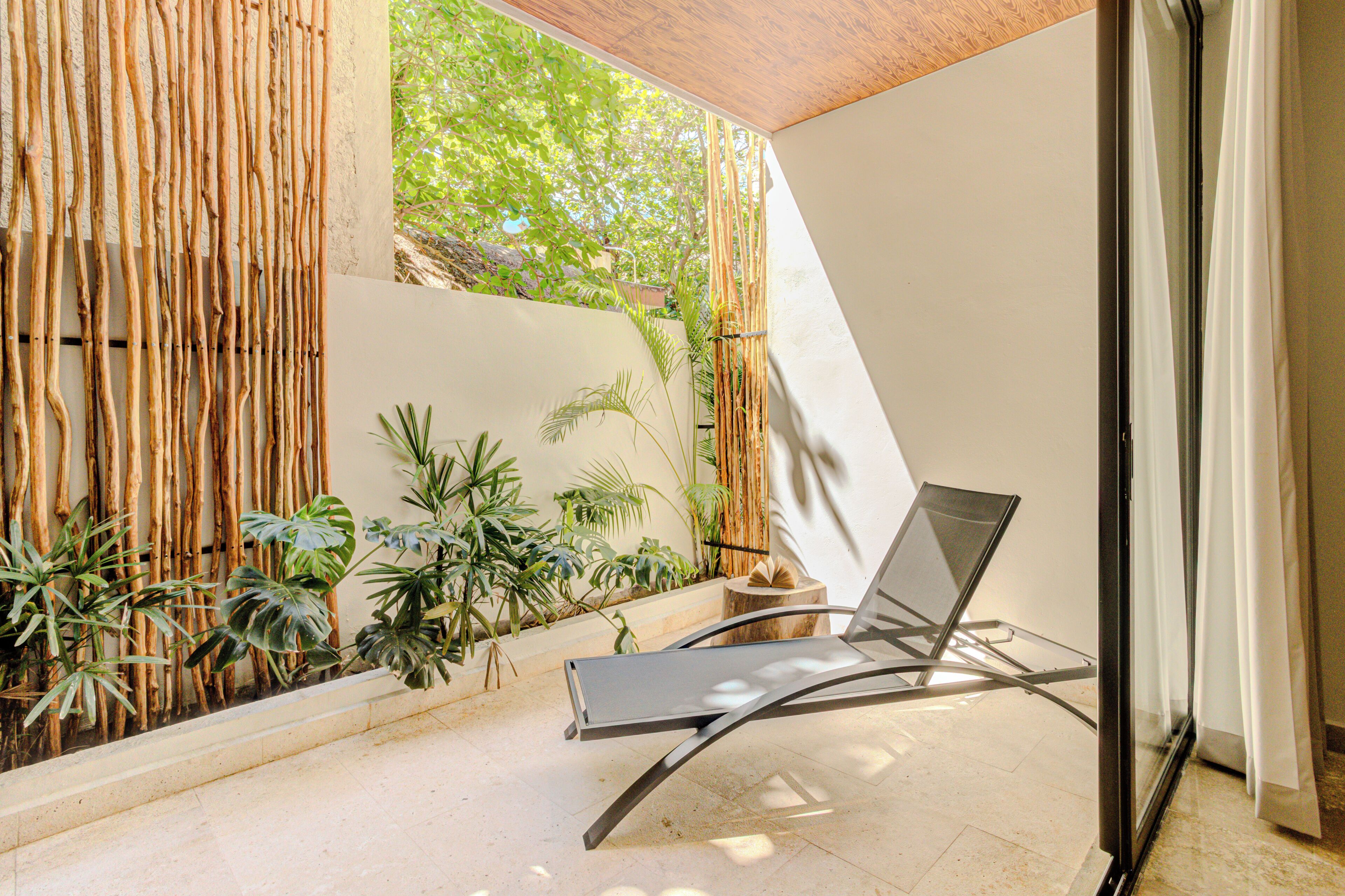 A modern outdoor seating area with a metal chair, bamboo wall, and various plants.
