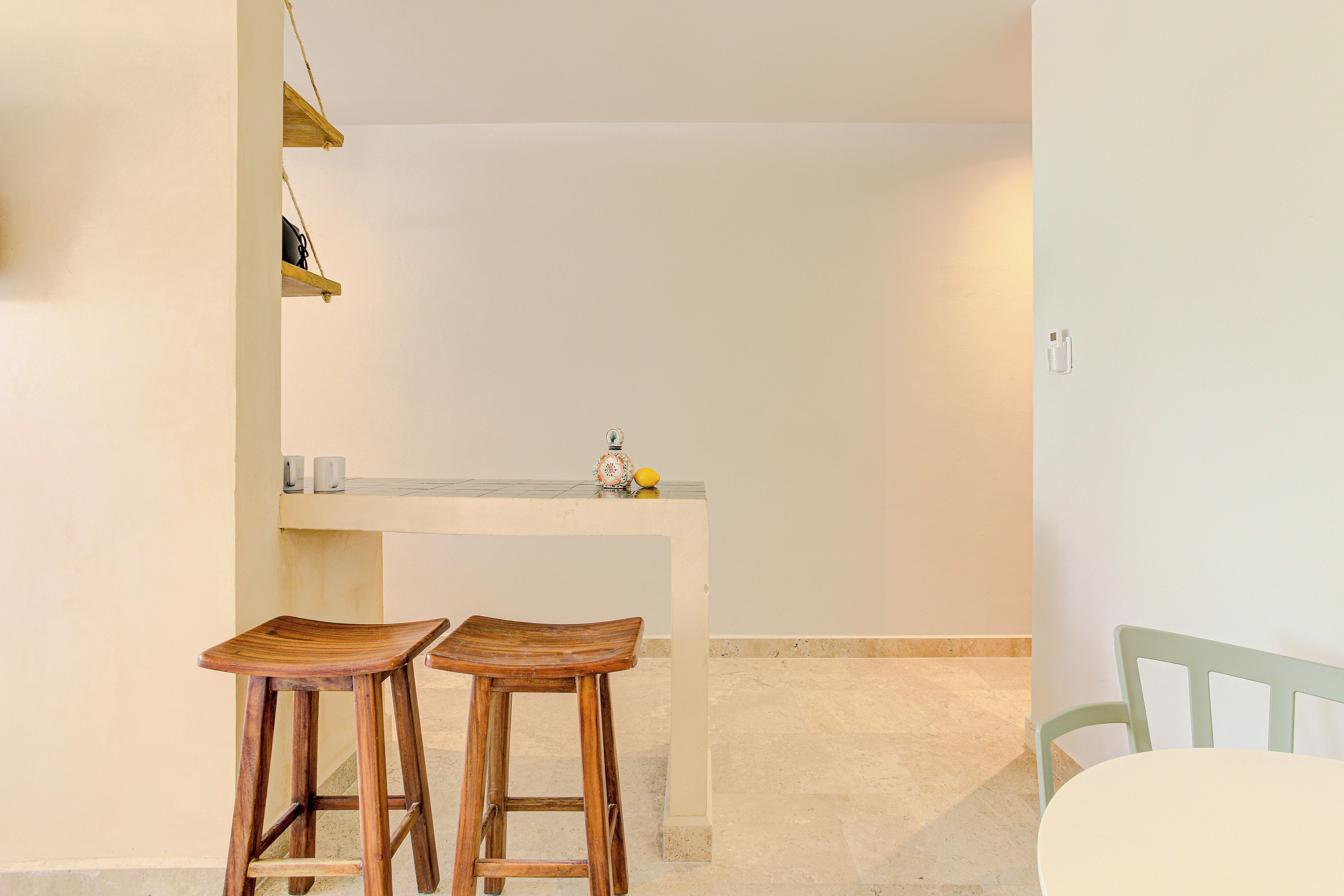A minimalist kitchen with a white countertop, two wooden stools, and a small table.