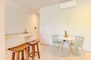 A minimalist room with a round table, two chairs, a small bar area, and an air conditioning unit.