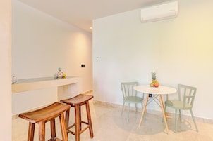 A minimalist room with a round table, two chairs, a small bar area, and an air conditioning unit.