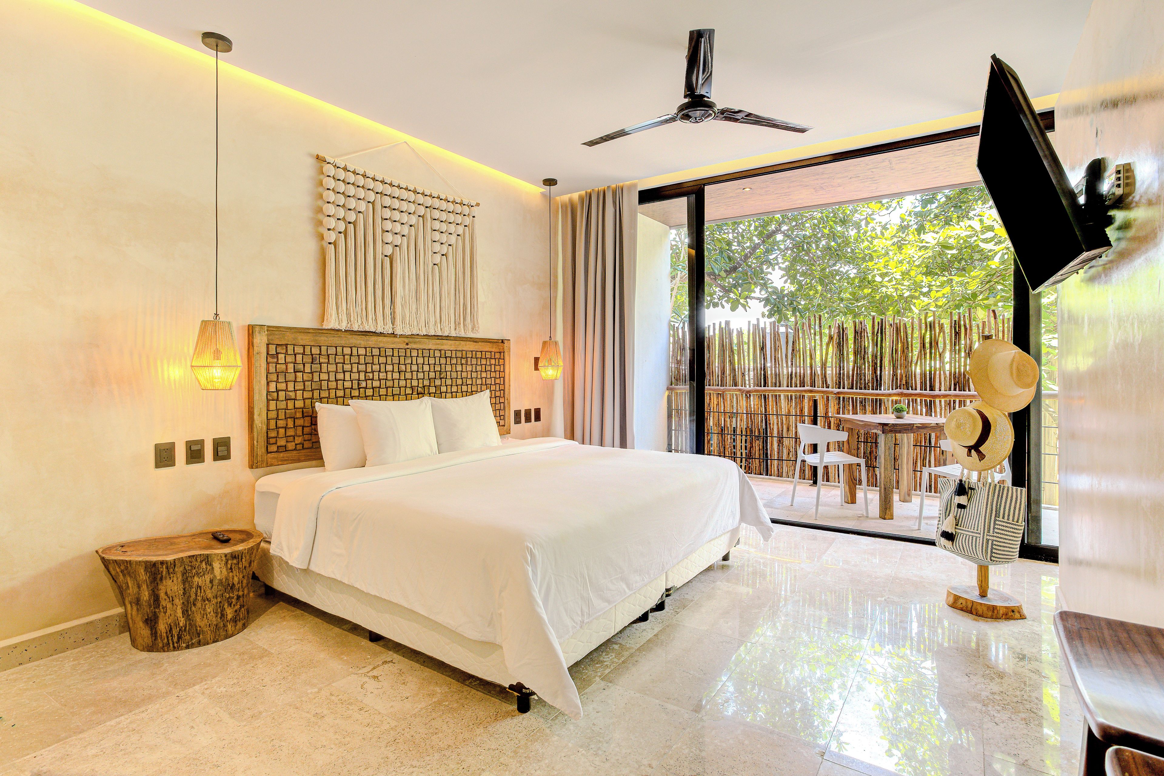 A hotel room with a bed, a ceiling fan, a wall-mounted TV, and a view of the outdoors.