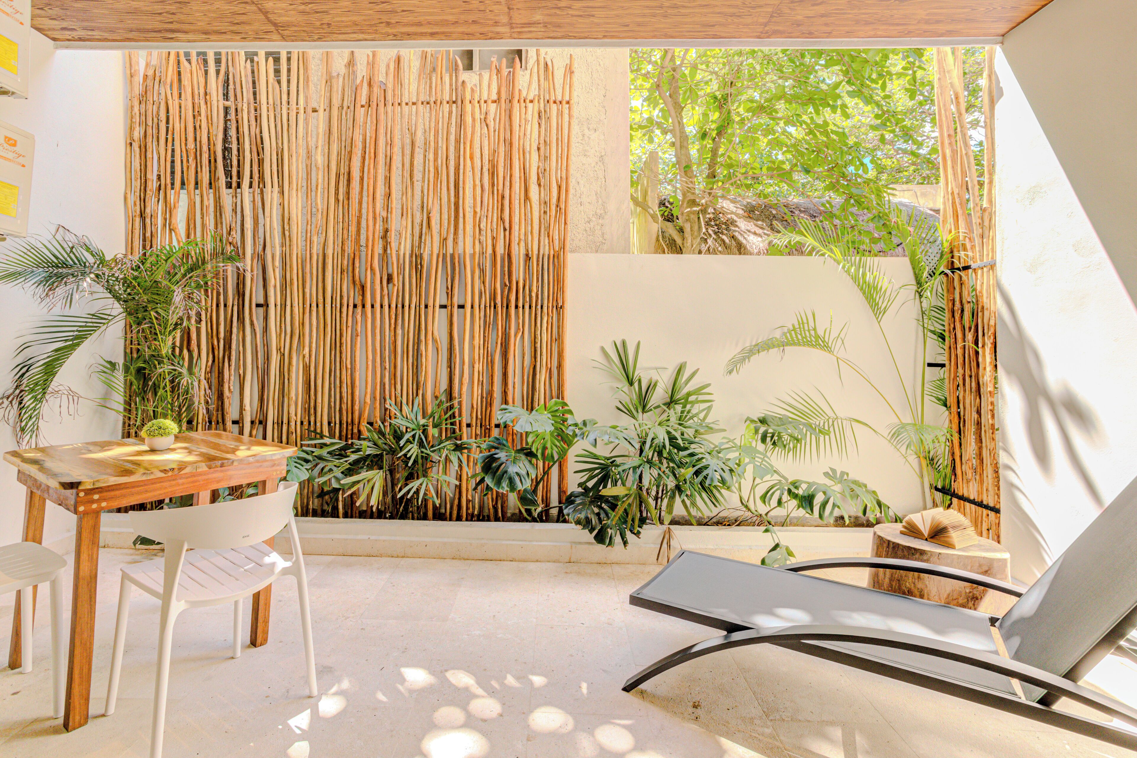 A modern outdoor seating area with a bamboo wall, a table, chairs, and a lounge chair.